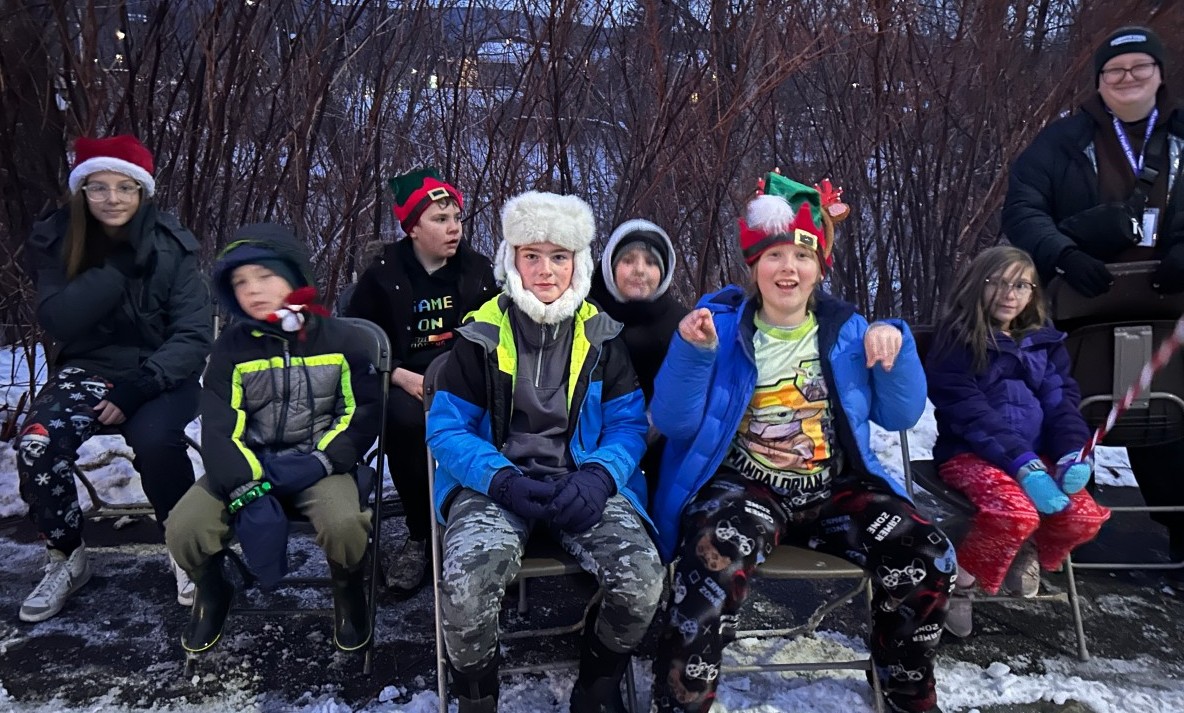 Children in winter, sitting outside, wearing winter and holiday hats.