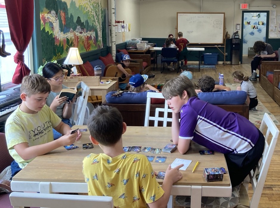 Youth in the main room, playing cards, guitar, drawing, reading, and writing.